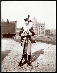 A man on a rooftop dressed in a traditional military uniform, holding a rifle